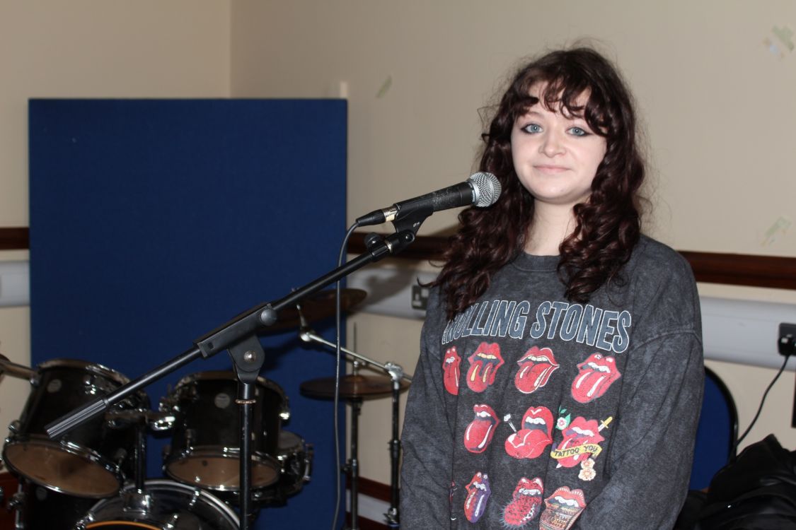 A student at a microphone with musical instruments in the background